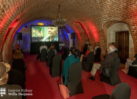 fotografia. projekcja filmu w ramach festiwalu art piknik. publiczność siedzi na owiniętych ciemnym materiałem krzesłach w niskiej, łukowato sklepionej, ceglanej sali w podziemiach willi decjusza.